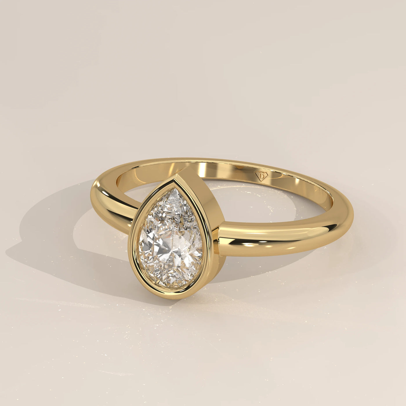 A solitaire pear-shaped diamond ring in a yellow gold bezel setting.