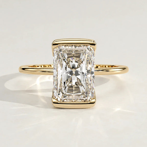 A radiant cut diamond engagement ring set in a yellow gold bezel.