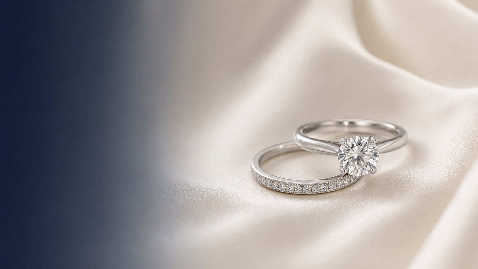 White-gold solitaire engagement ring and pavé wedding band resting on ivory silk with navy space for the article title