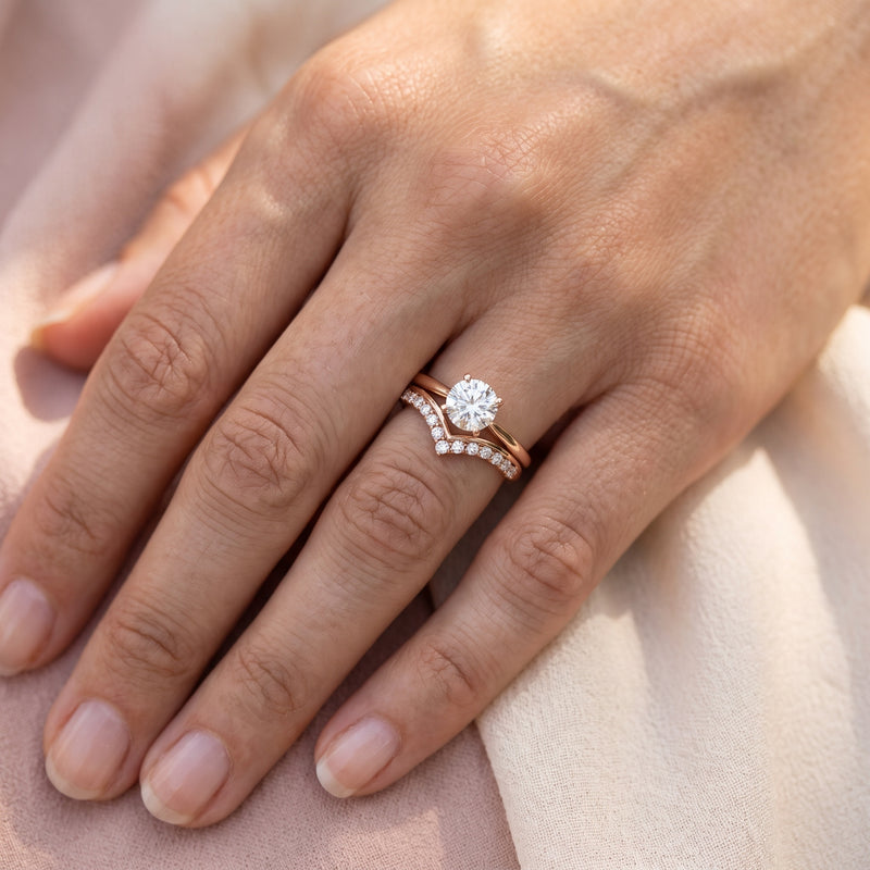 Curved rose gold diamond band nested against a solitaire engagement ring
