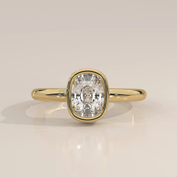 A yellow gold ring with a bezel-set cushion-cut diamond.