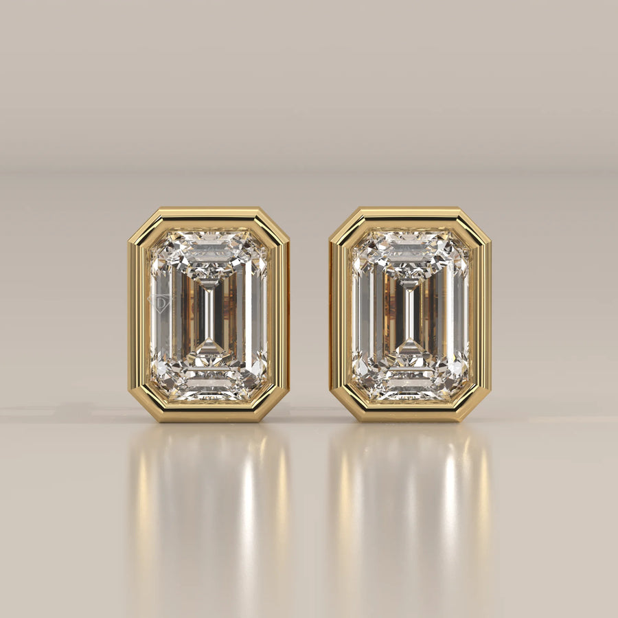 A pair of emerald-cut diamond stud earrings in a yellow gold bezel setting.