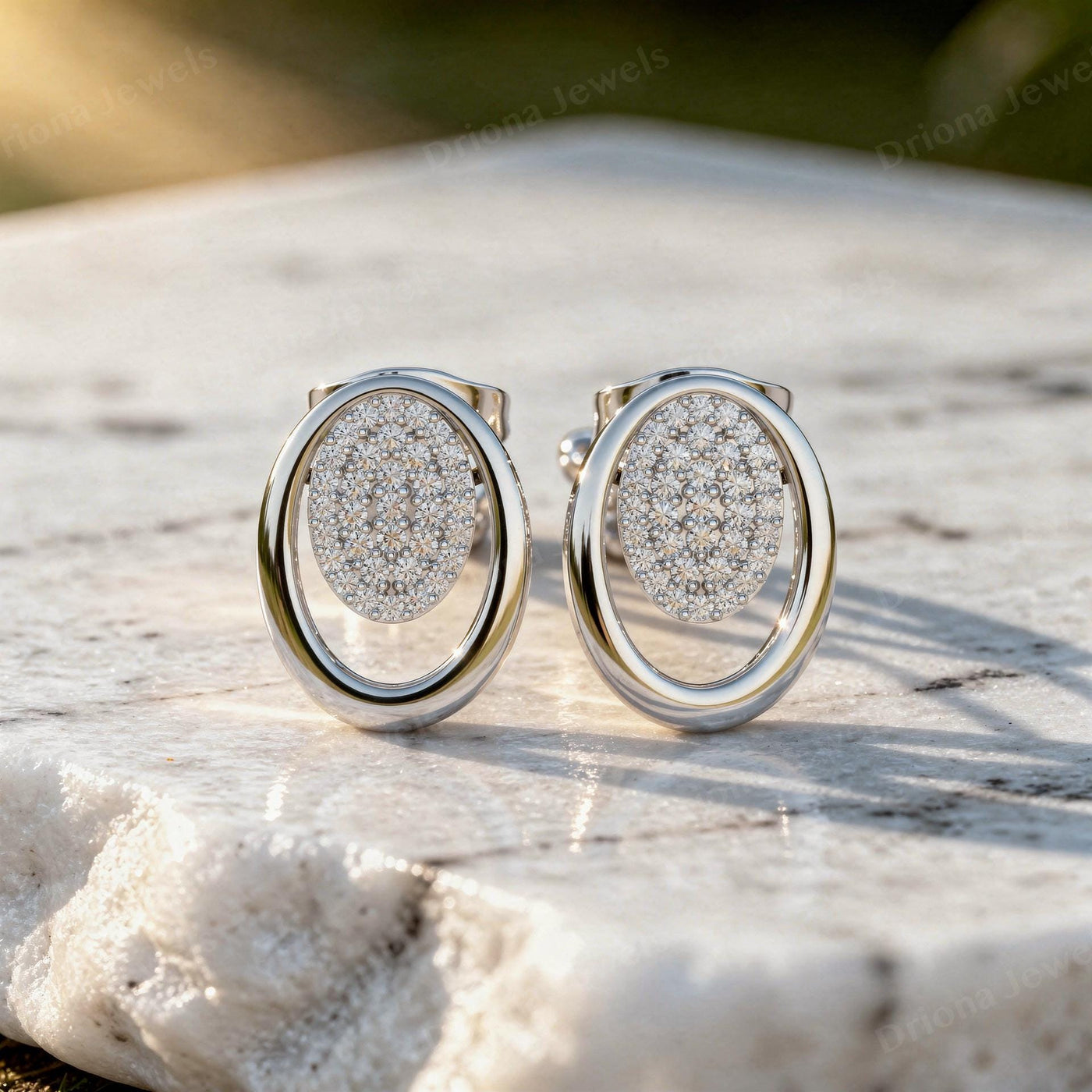 Oval pave diamond stud earrings in a solid gold open-frame design on a white stone surface.