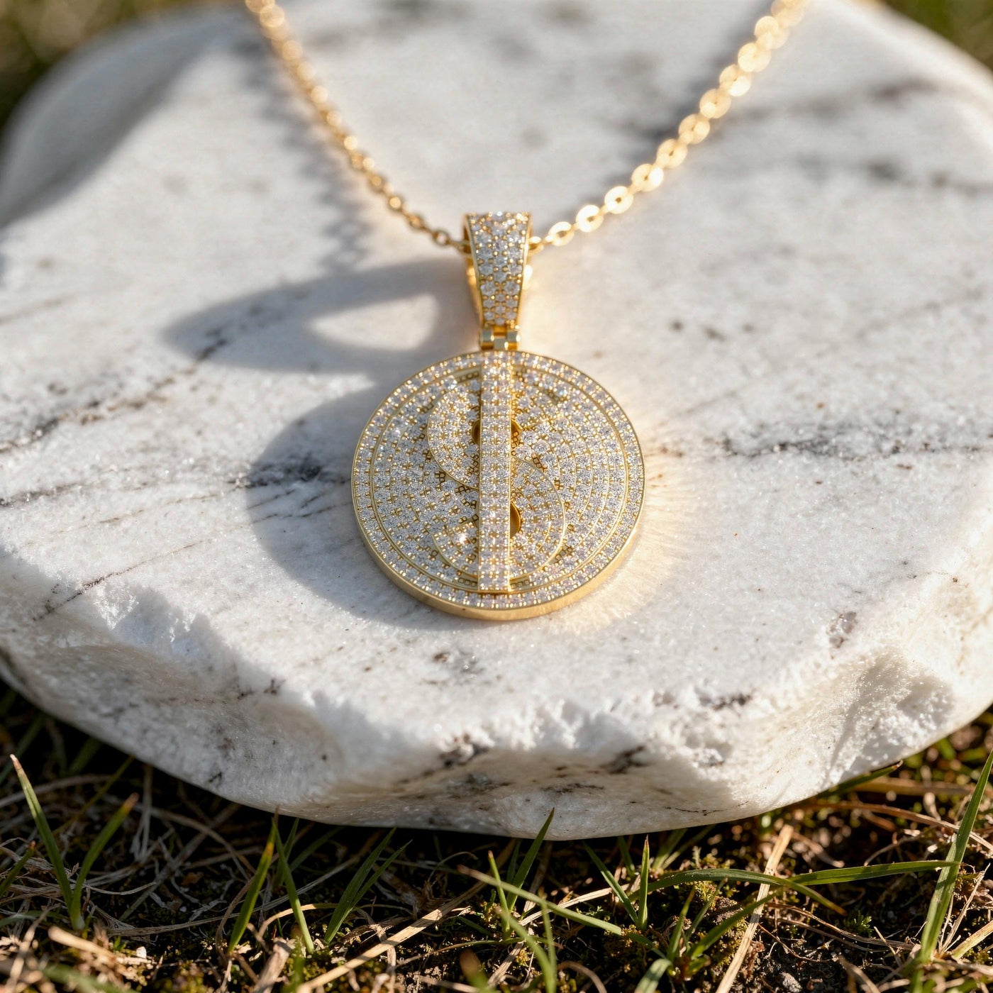Iced dollar sign diamond medallion in 14K rose gold on a gold chain over a white marble stone.