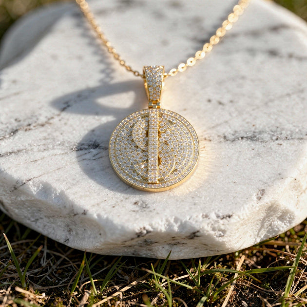 Iced dollar sign diamond medallion in 14K rose gold on a gold chain over a white marble stone.