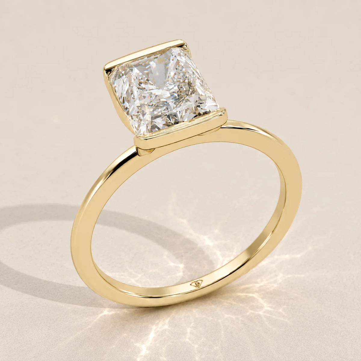 A 14k yellow gold ring with a radiant cut diamond in a bezel setting.