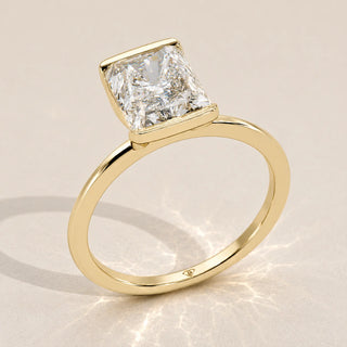 A 14k yellow gold ring with a radiant cut diamond in a bezel setting.