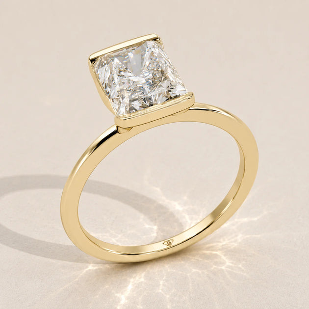 A 14k yellow gold ring with a radiant cut diamond in a bezel setting.