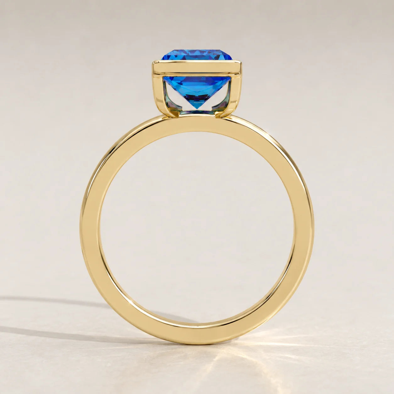 A yellow gold ring with a cushion-cut blue gemstone set in a bezel.