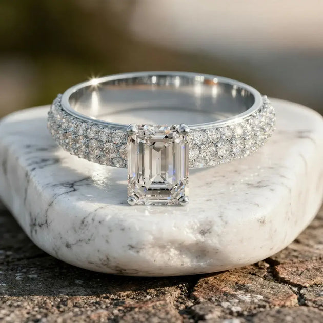 Emerald cut lab grown diamond engagement ring with a triple-row pavé diamond band on a white stone.
