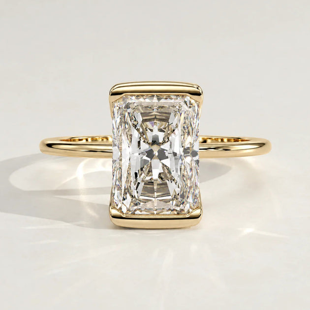 A radiant cut diamond engagement ring set in a yellow gold bezel.