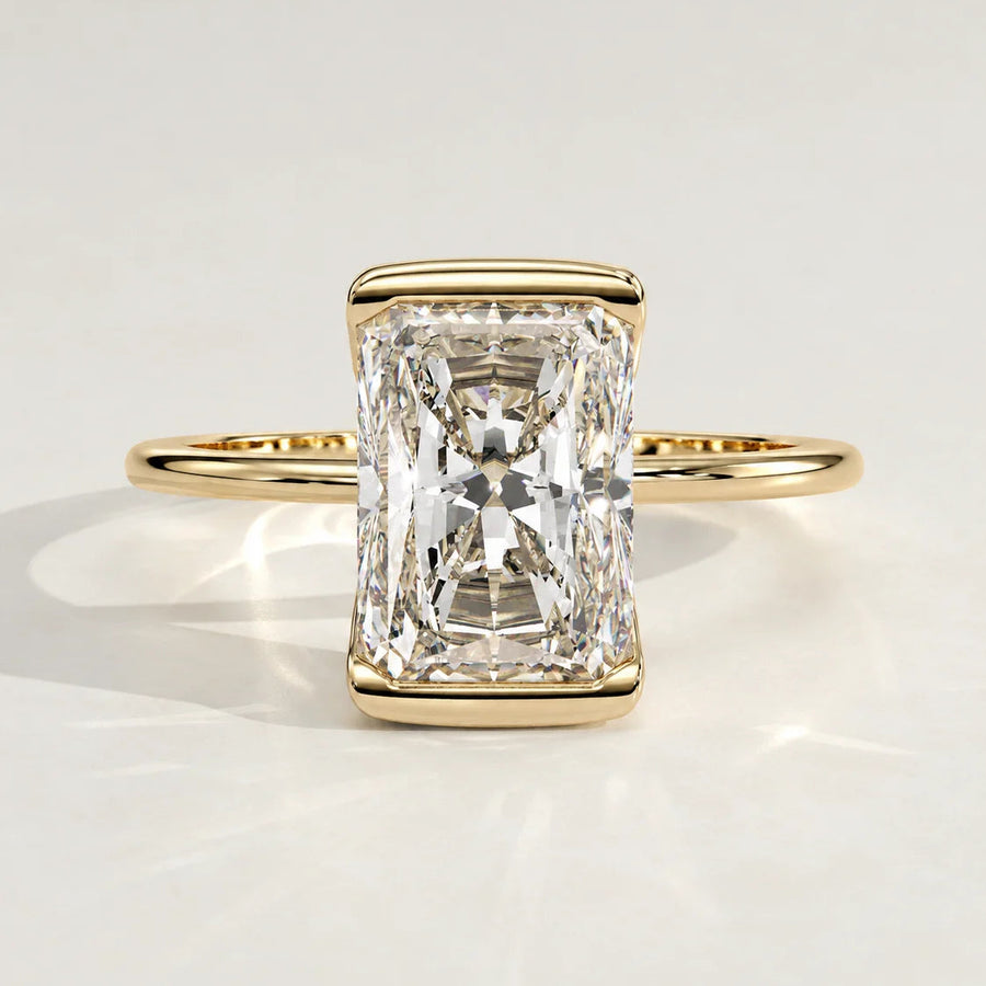 A radiant cut diamond engagement ring set in a yellow gold bezel.
