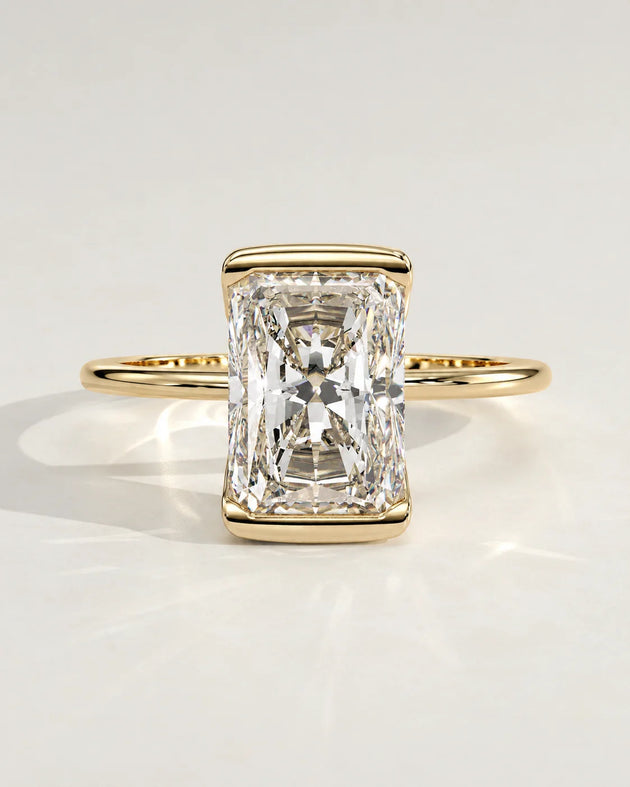 A radiant cut diamond engagement ring set in a yellow gold bezel.